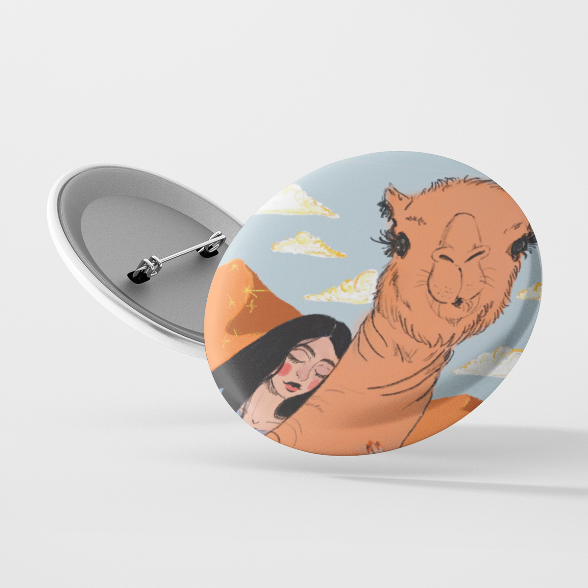 A circular pin with a depiction of a woman riding a camel in a desert landscape with blue sky and white clouds.