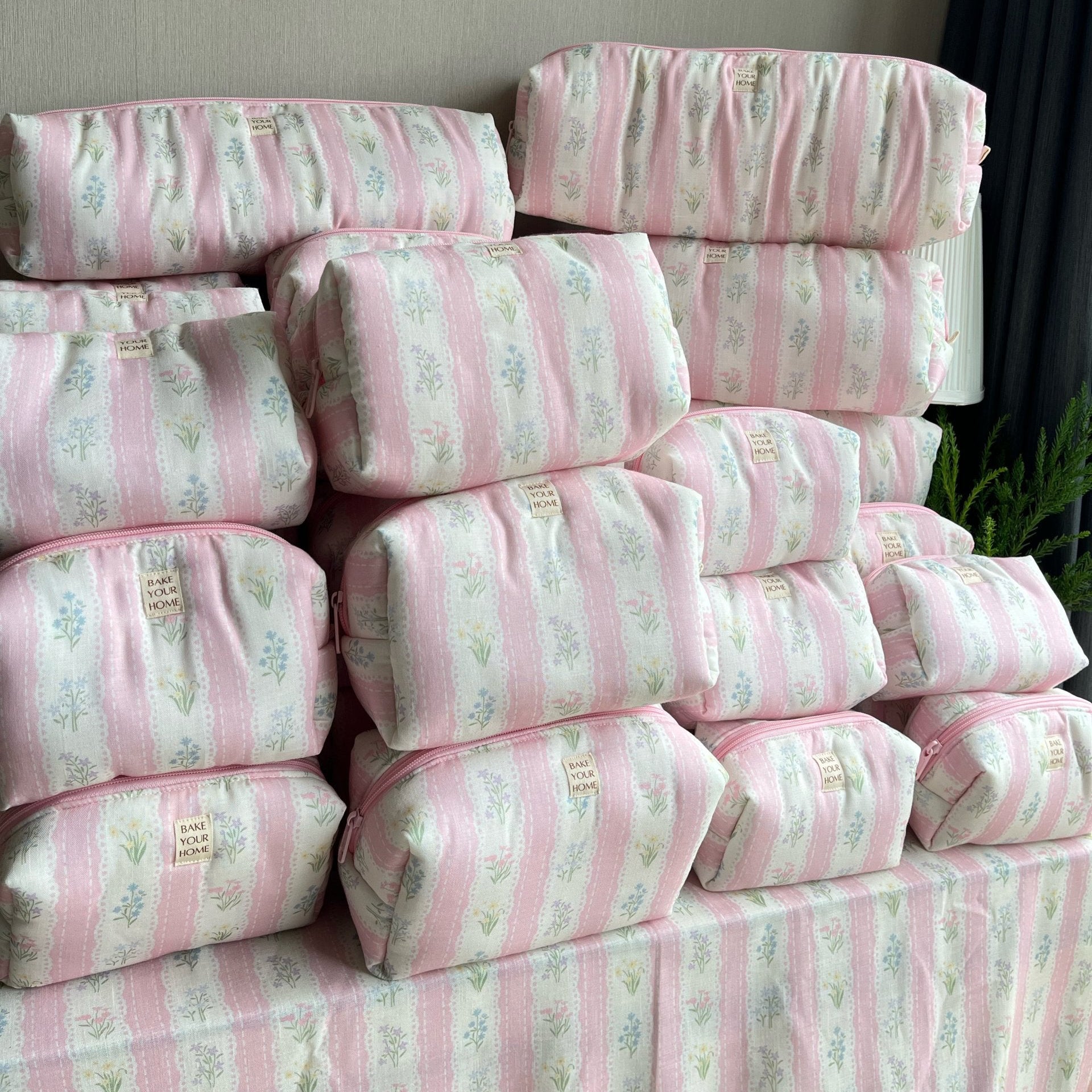 A stack of pink and white striped fabric pouches with a delicate floral print, arranged on a matching fabric-covered surface against a neutral indoor wall.