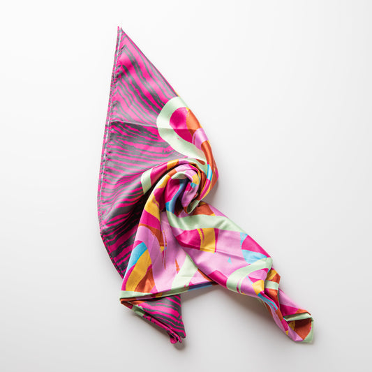 A lightweight silk scarf with a vibrant abstract print in pink, orange, yellow, and green, styled in a loose knot on a clean white background.