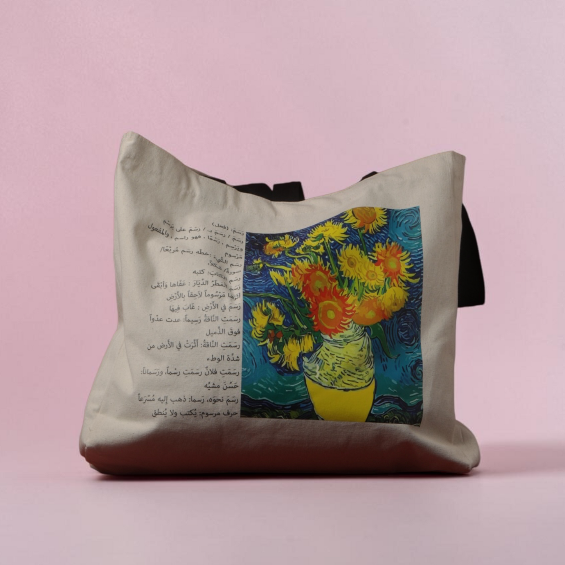 A canvas tote bag with black handles, featuring a split design: one side has black Arabic text, and the other side displays a colorful print of Van Gogh's 'Venus in a Mirror' style painting with yellow flowers and blue background. The bag is set against a solid light pink studio background.